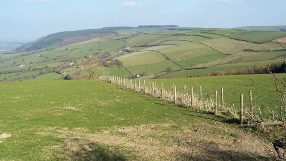 Rolling green hills, a fence, and a distant village.