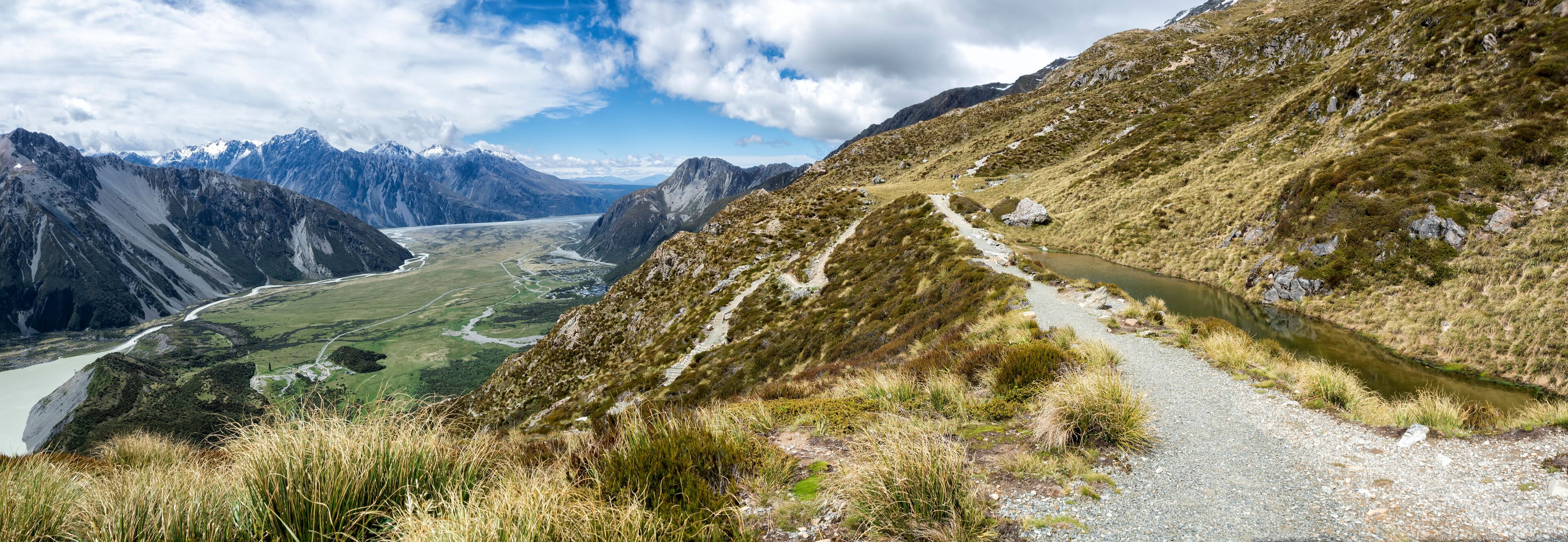 A mountain landscape with a river, a hiking trail, and a valley.