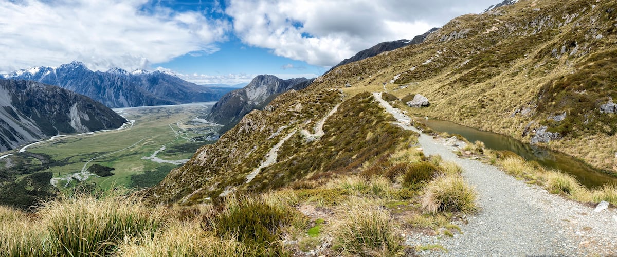 A mountain landscape with a river, a hiking trail, and a valley.