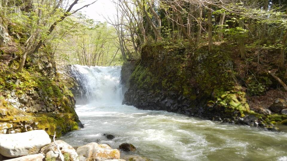 A waterfall surrounded by lush greenery and rocky terrain.