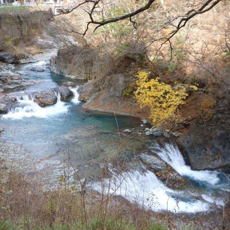 A river flowing through a rocky landscape with a waterfall and yellow foliage.