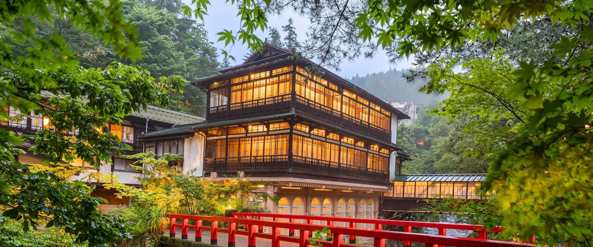 A traditional Japanese building with a red bridge in a lush, green setting.
