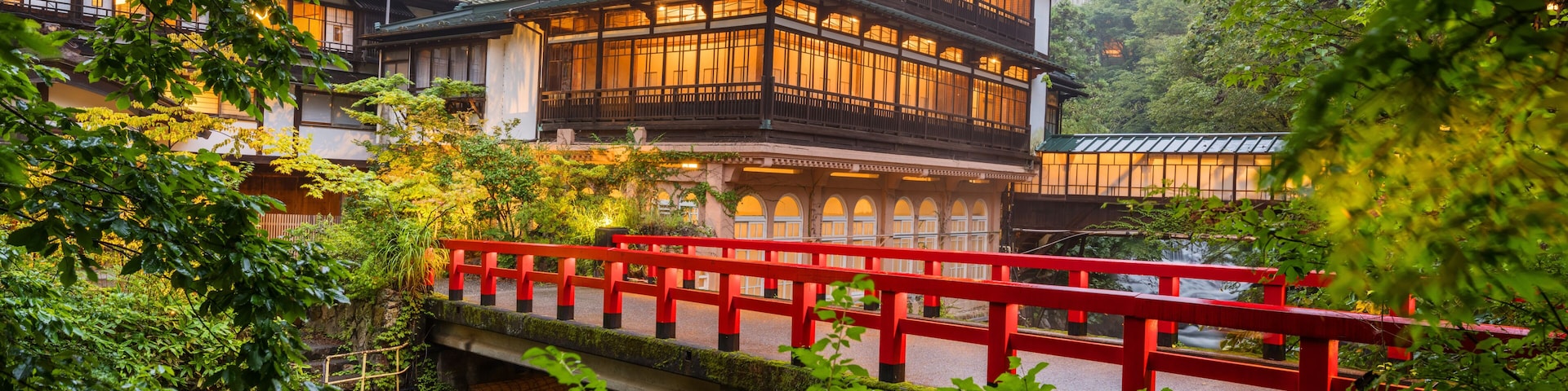 A traditional Japanese building with a red bridge in a lush, green setting.
