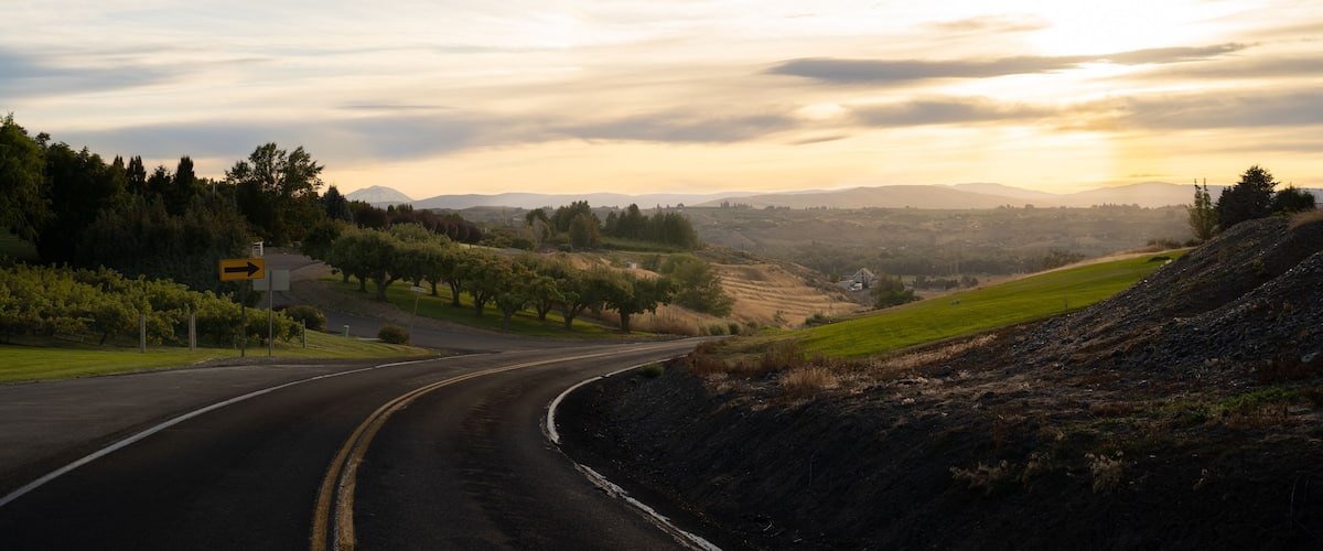 A winding road curving through a hilly landscape with a sunset in the background.