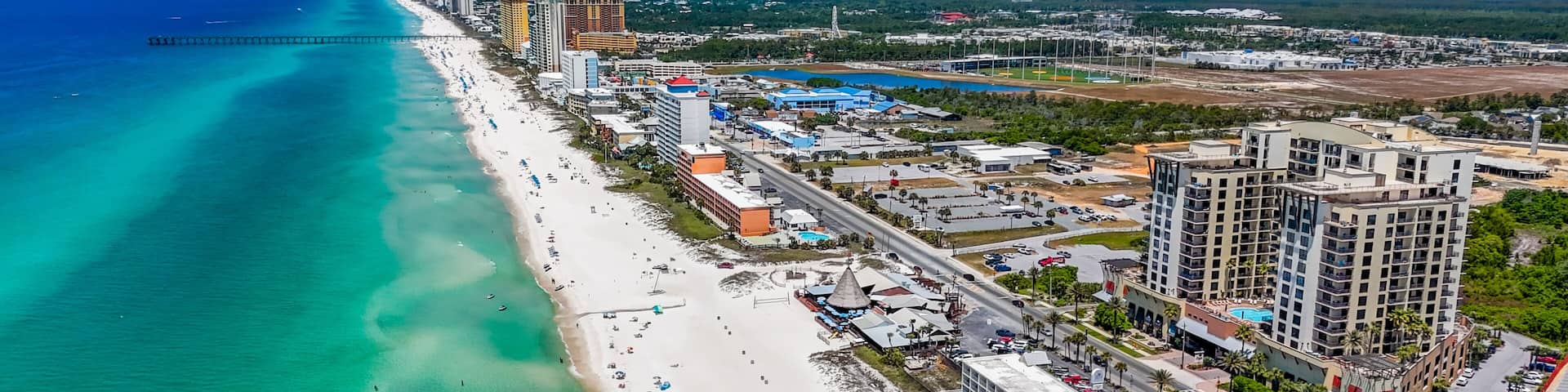 A coastal cityscape with a long beach, clear turquoise waters, and high-rise buildings.