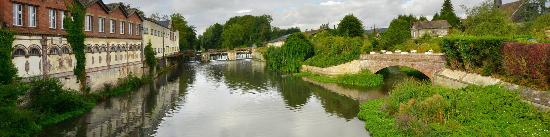 A river with a bridge, buildings, and greenery.