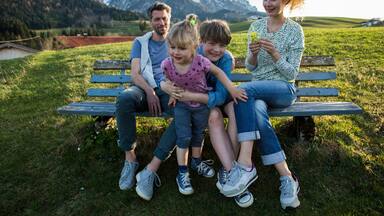Austria, Tyrol, Walchsee, happy family resting on a bench in the mountains