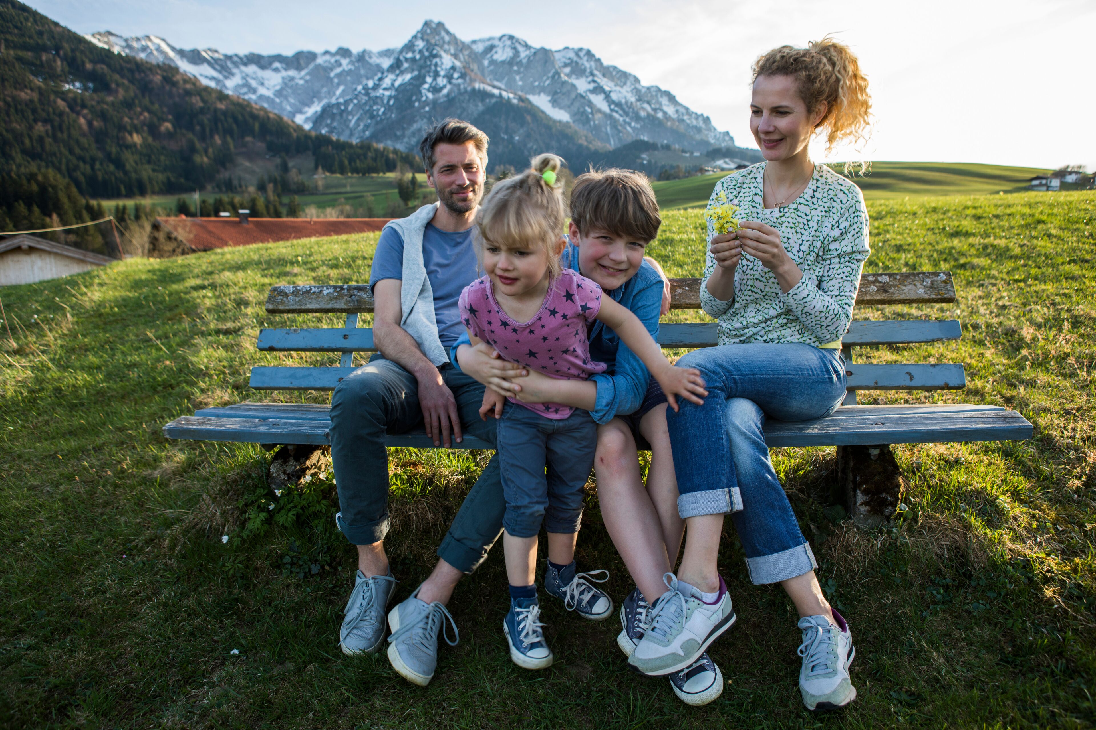 A family on a bench with a mountainous landscape in the background.