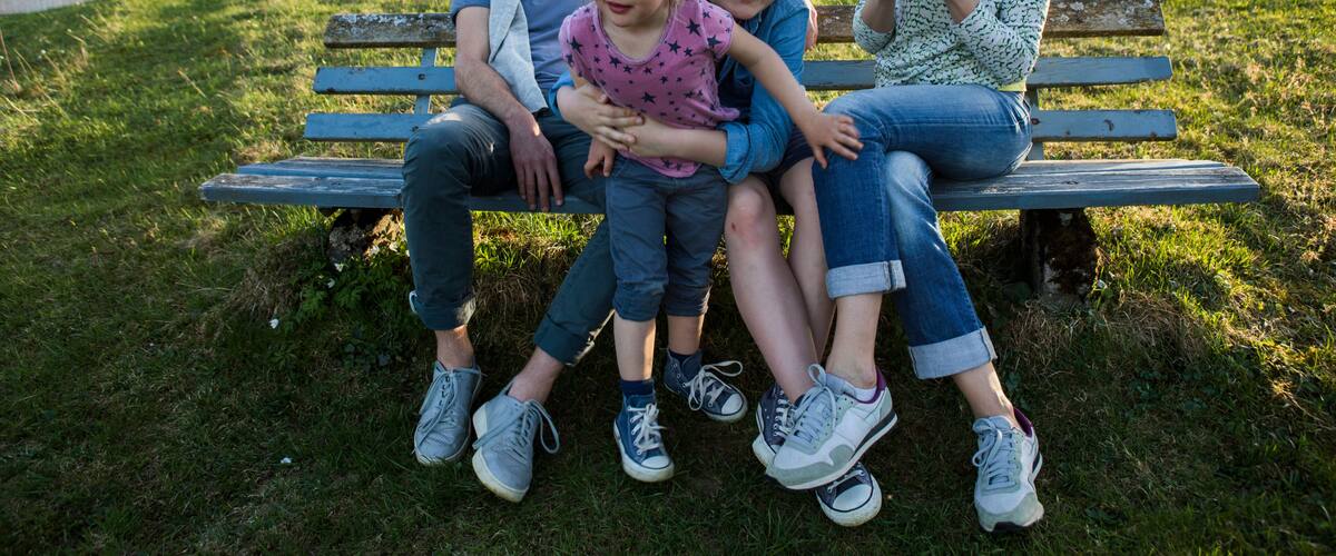 A family on a bench with a mountainous landscape in the background.