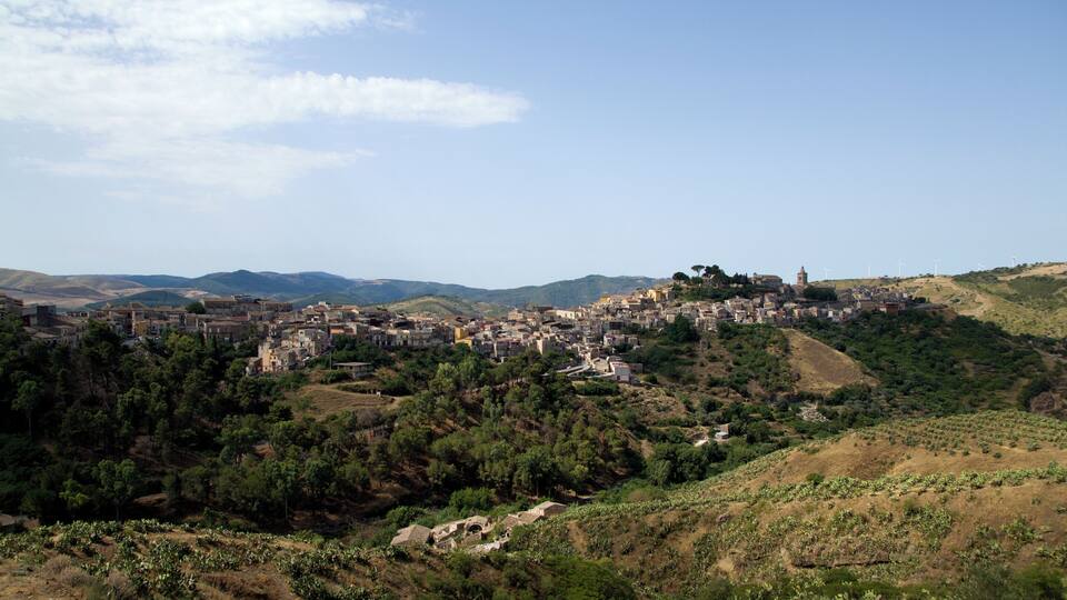A town nestled in a valley with a backdrop of hills and wind turbines.