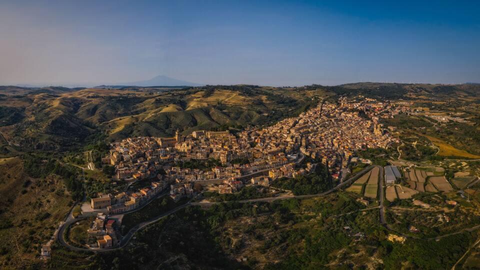 An aerial view of a town nestled in hilly terrain with a prominent church and winding roads.