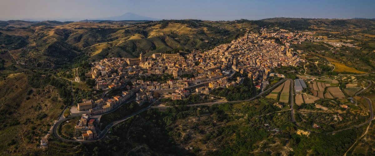 An aerial view of a town nestled in hilly terrain with a prominent church and winding roads.