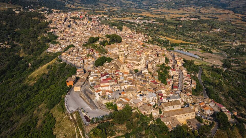 An aerial view of a historic town with winding roads, dense architecture, and surrounding hills.