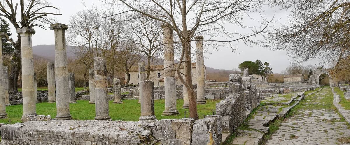 Ancient stone columns and ruins in a grassy area with a cobblestone path.