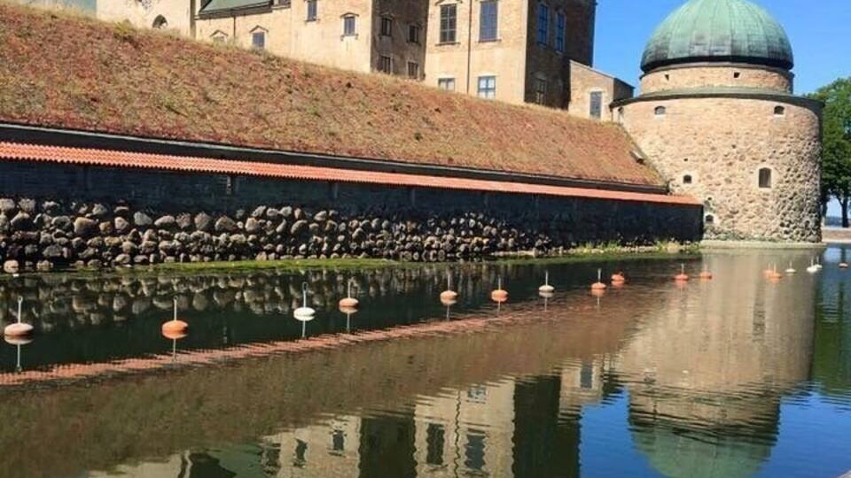 A historic building with two domes and a stone tower, reflecting in a calm body of water.