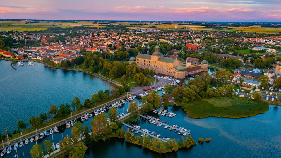 A lakeside town with a prominent castle, marina, and surrounding greenery.