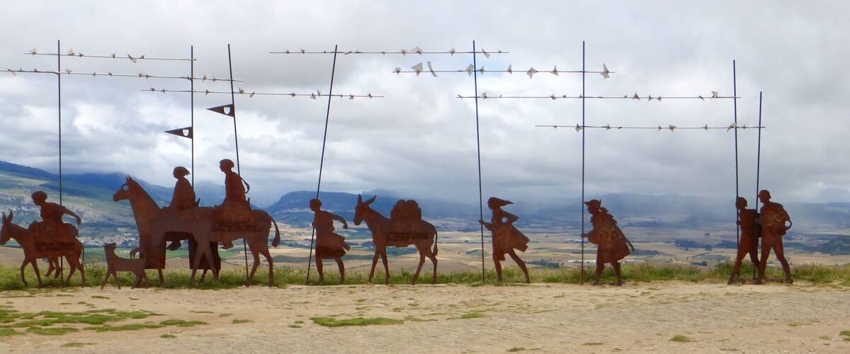A sculpture of people on horses in a field with barbed wire and flowers.