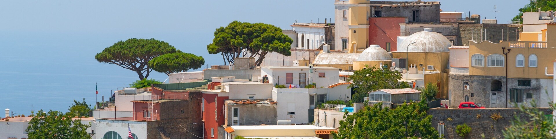 A coastal town with Mediterranean architecture, including a church with a bell tower, and lush greenery.