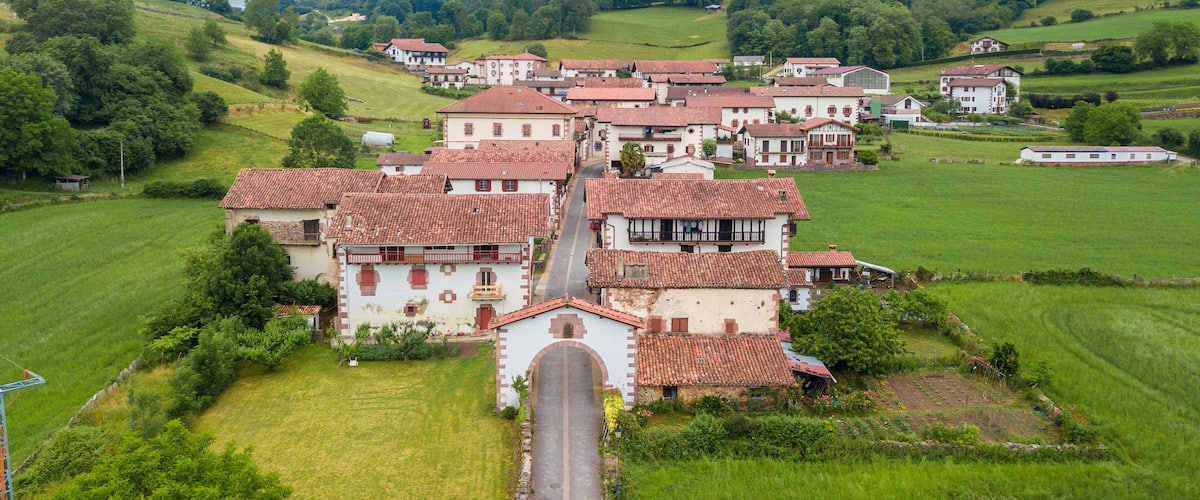 A village with terracotta-roofed houses surrounded by lush green fields and rolling hills.