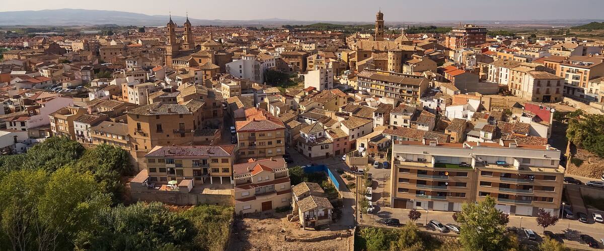 A densely packed urban area with historic buildings, a prominent church with two towers, and a clear view of distant mountains.