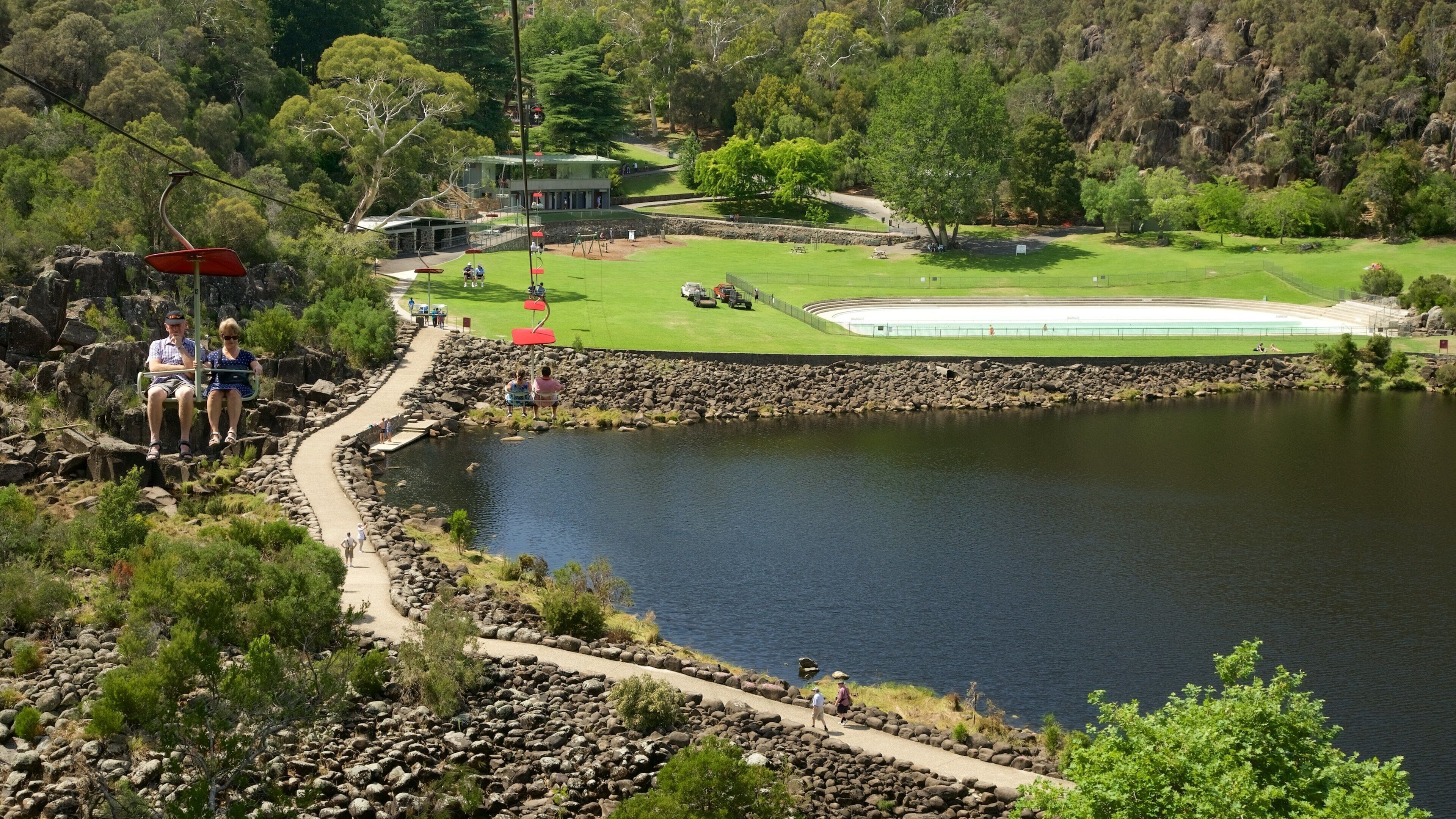 A lake surrounded by rocks and greenery, with a golf course and a building in the background.