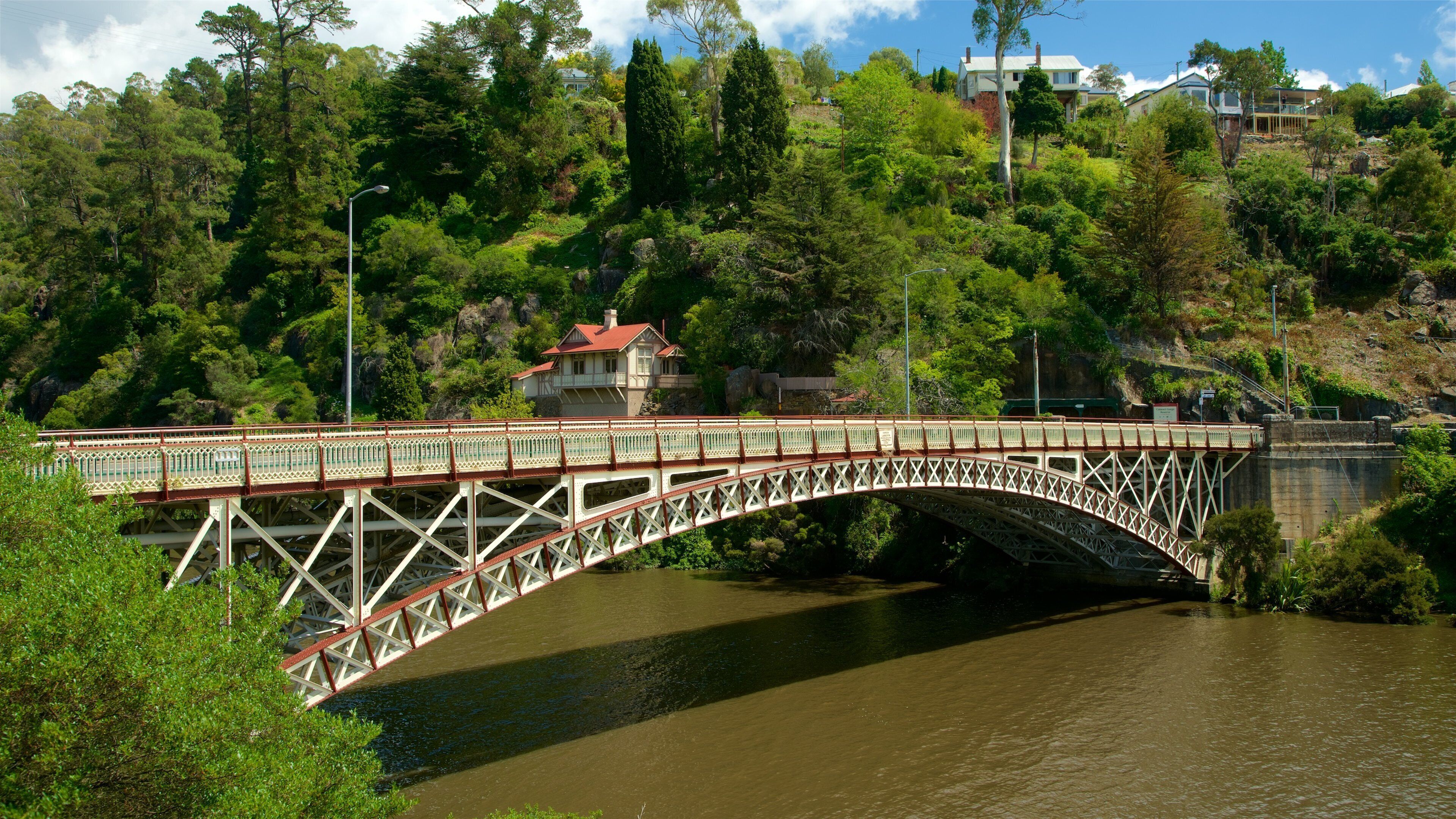 A bridge over a river with a house on a hill in the background.
