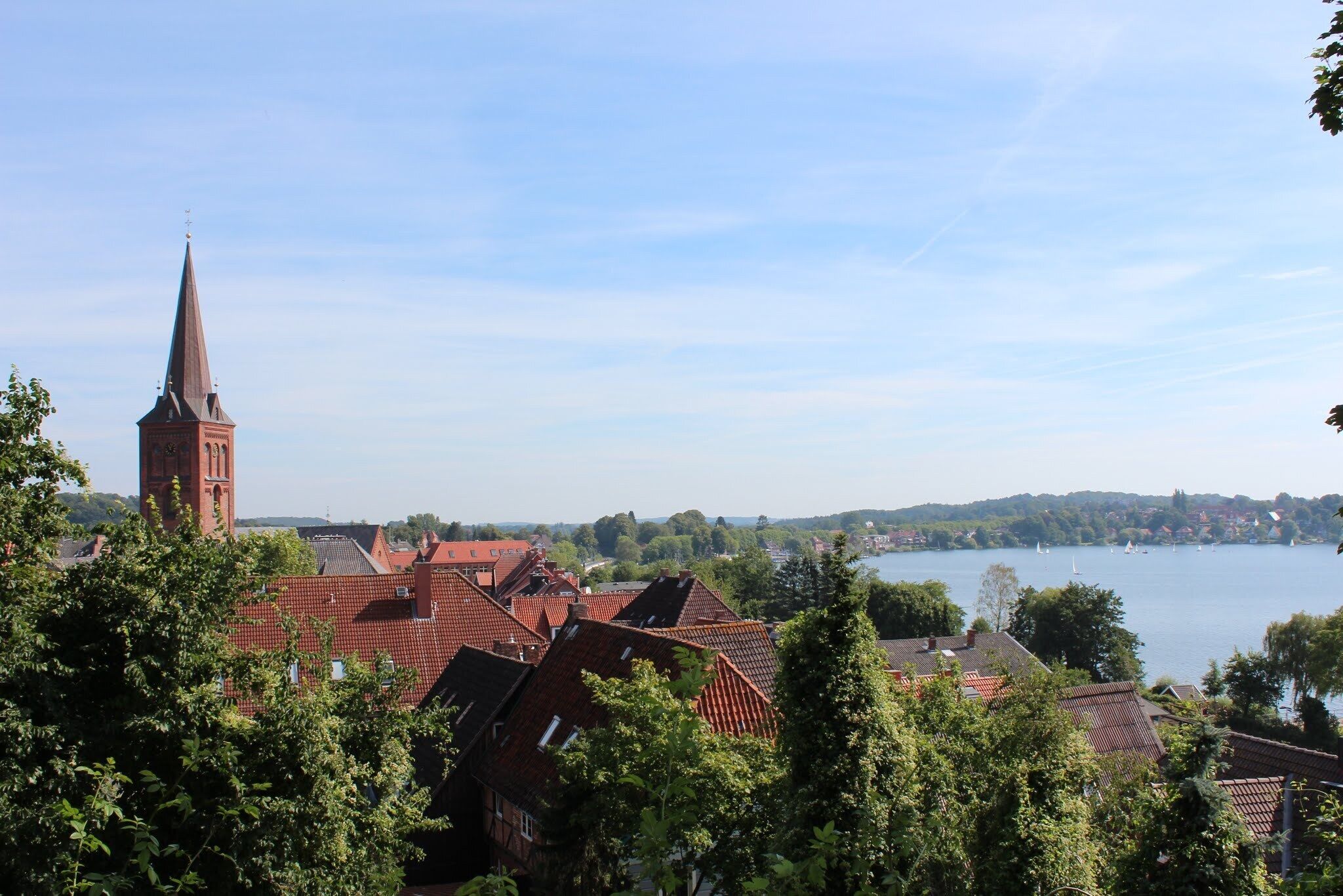 A town with a prominent church tower, red-roofed buildings, and a lake with sailboats.