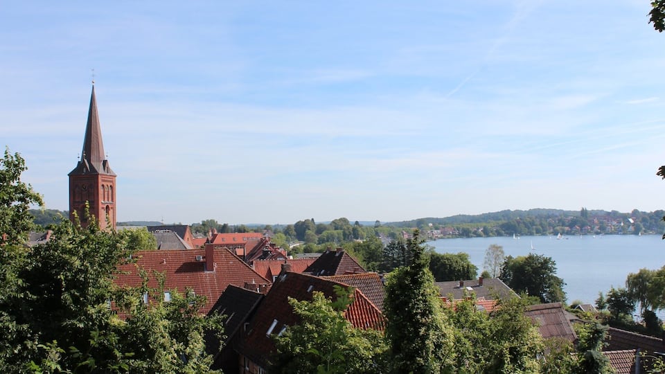 A town with a prominent church tower, red-roofed buildings, and a lake with sailboats.