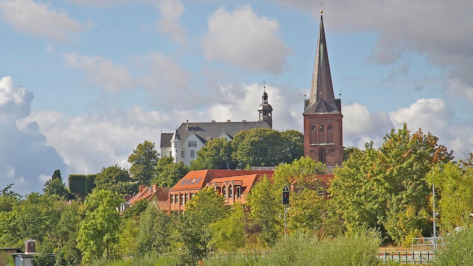 A river with a church and residential buildings in the background.