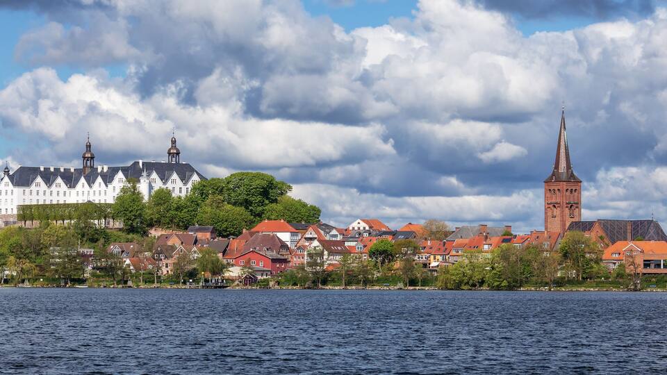 A lakeside town with a prominent church tower and a large white building with multiple spires.