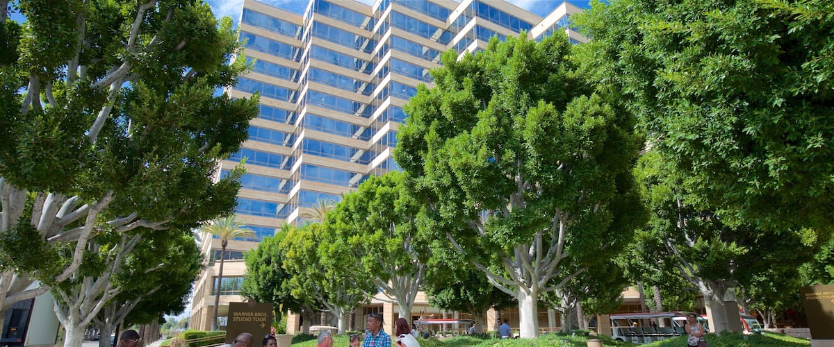 A group of people near a Warner Bros. Studio Tour sign, with a modern building and trees in the background.