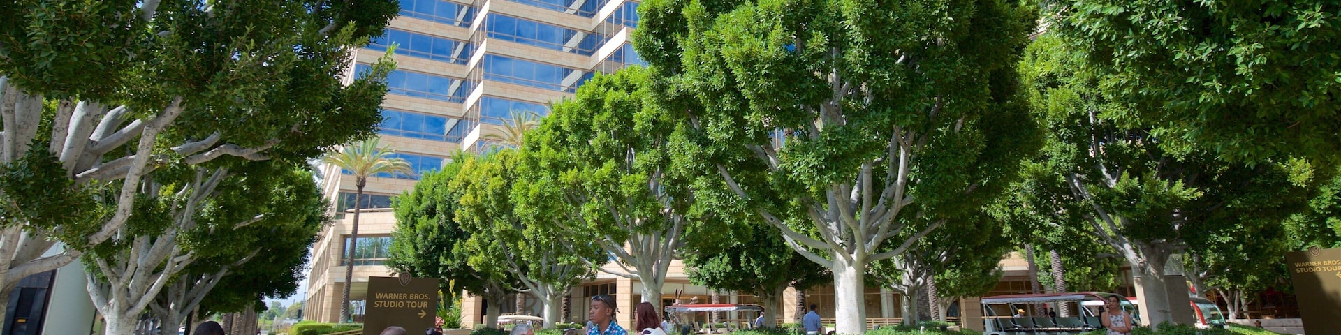 A group of people near a Warner Bros. Studio Tour sign, with a modern building and trees in the background.
