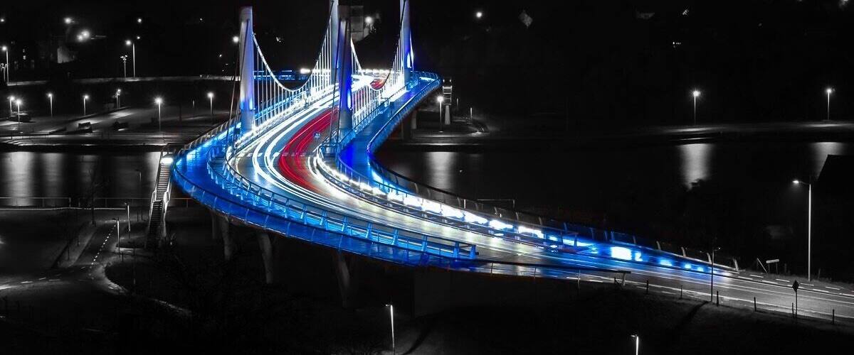 A nighttime view of a curved bridge with blue lighting and a red road.