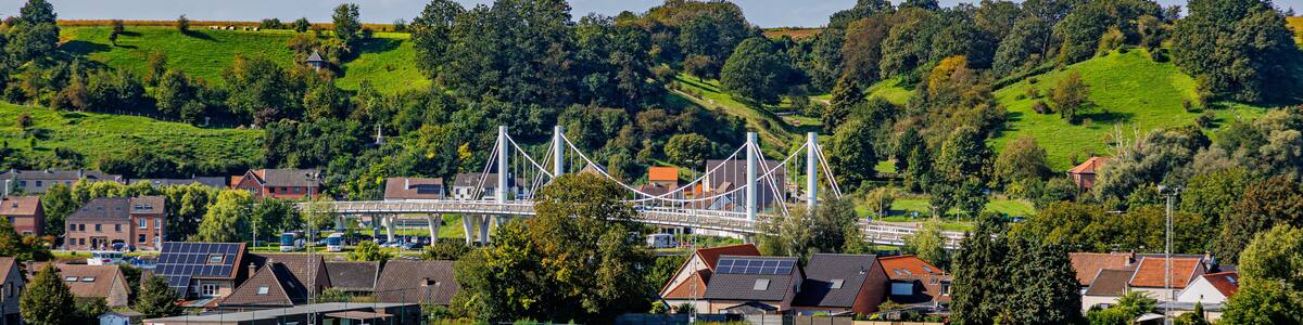 Caestert plateau with green esplanade, suspension bridge, Kanne village and hill with green leaf trees in background, Belgian agricultural land with sown land, sunny day in Riemst, Belgium