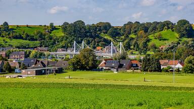 Caestert plateau with green esplanade, suspension bridge, Kanne village and hill with green leaf trees in background, Belgian agricultural land with sown land, sunny day in Riemst, Belgium