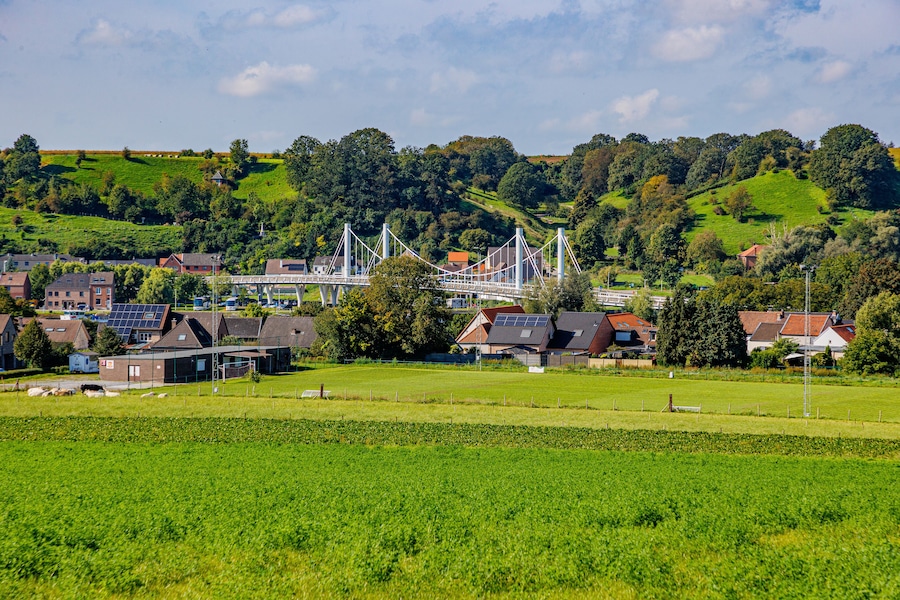 Caestert plateau with green esplanade, suspension bridge, Kanne village and hill with green leaf trees in background, Belgian agricultural land with sown land, sunny day in Riemst, Belgium