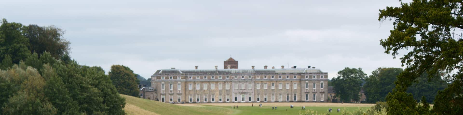 A large historic building surrounded by a lake and dense trees.