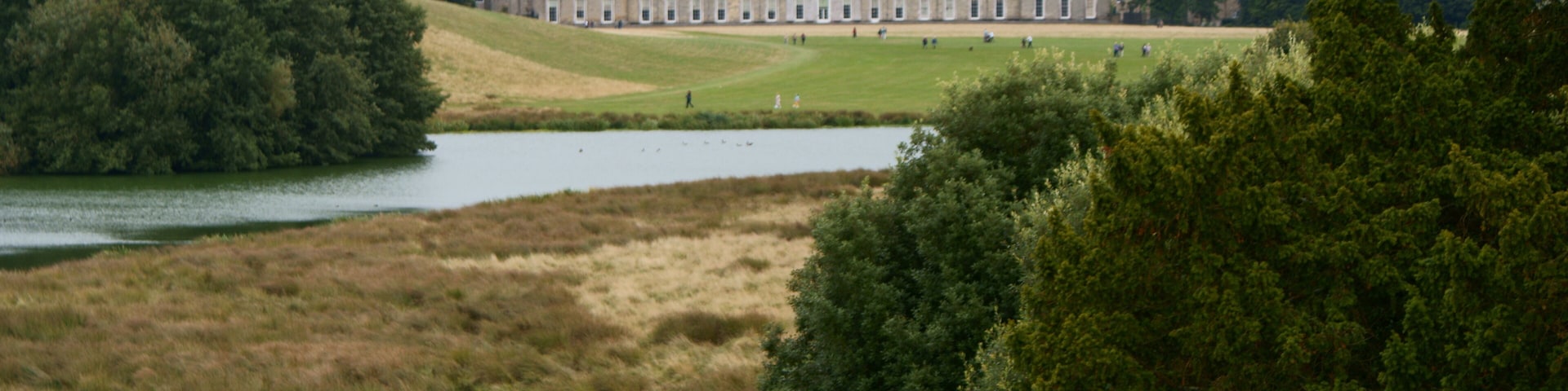 Ein großes, historisches Gebäude, umgeben von einem See und dichter Baumlandschaft.