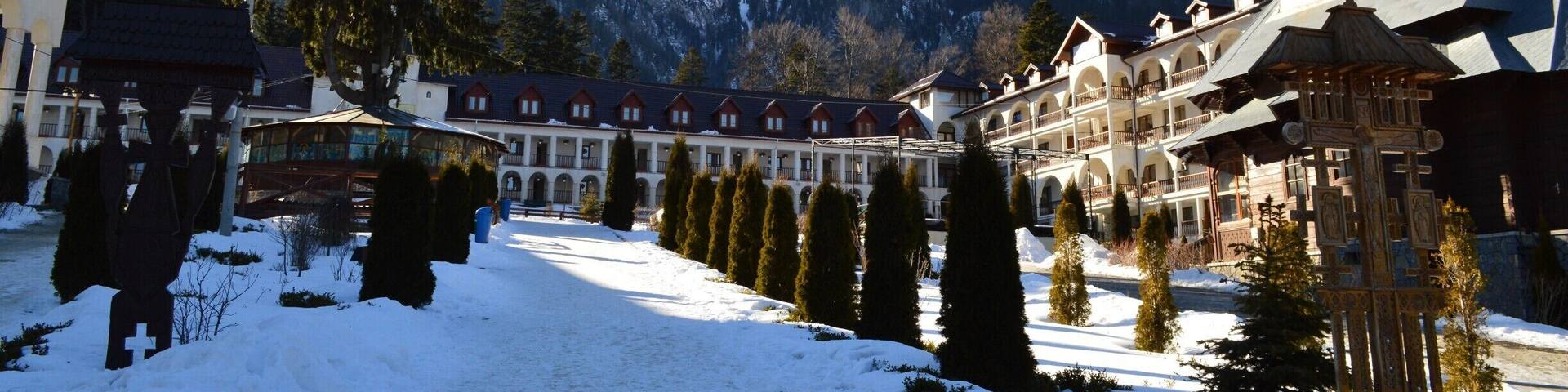 Caraiman Monastery is an orthodox monastery, which is situated in town Buşteni, Prahova district, at the foot of the massif Caraiman. The Cross from above the Caraiman seems to guard the path, which leeds the steps of the pilgrims towards the monastery. Going towards the cab from Buşteni, at a time, on the left side, there are an indicator and an icon showing the path with stone tiles in patches, path leading towards the monastery.
The secretly like walking path, under the dark crowns of the fir trees is eventually reaching an oasis of light, the massif Caraiman emerges in all its splendour. In this glade, Father Gherontie Puiu built, by the grace of Lord and with Virgin’s Mary help, a great monastery.
Buşteni is a small mountain town situated in the northern part of Prahova district, Muntenia, located in the center of Romania. It is situated on the Prahova Valley, at he foot of the Bucegi Mountains, which have the maximum altitude of 2.505 m. Situated at a distance of 135 km from Bucharest, it stretches about 7 km along the Prahova Valley, between the “Deer Ford” and the tunnel dug into the mountain spur “Long Edge”.
The average height of the town Buşteni is of 850 m. It is one of the most popular mountain resorts, offering spectacular views, a lot of opportunities and holiday activities from skiing to hiking. It’s got a population of 10.463 inhabitants.
The Caraiman Monastery is situated at a height of about 900 m, being one of the highest altitudes where a place of worship has ever been built in our country.