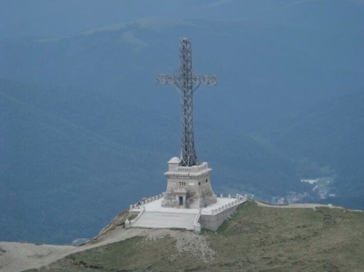 A cross monument on a hill with a coastal background.