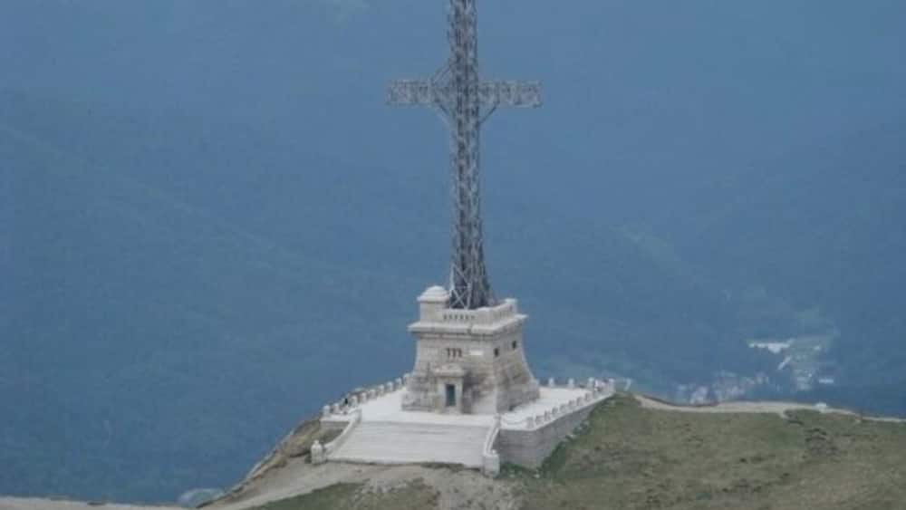 A cross monument on a hill with a coastal background.