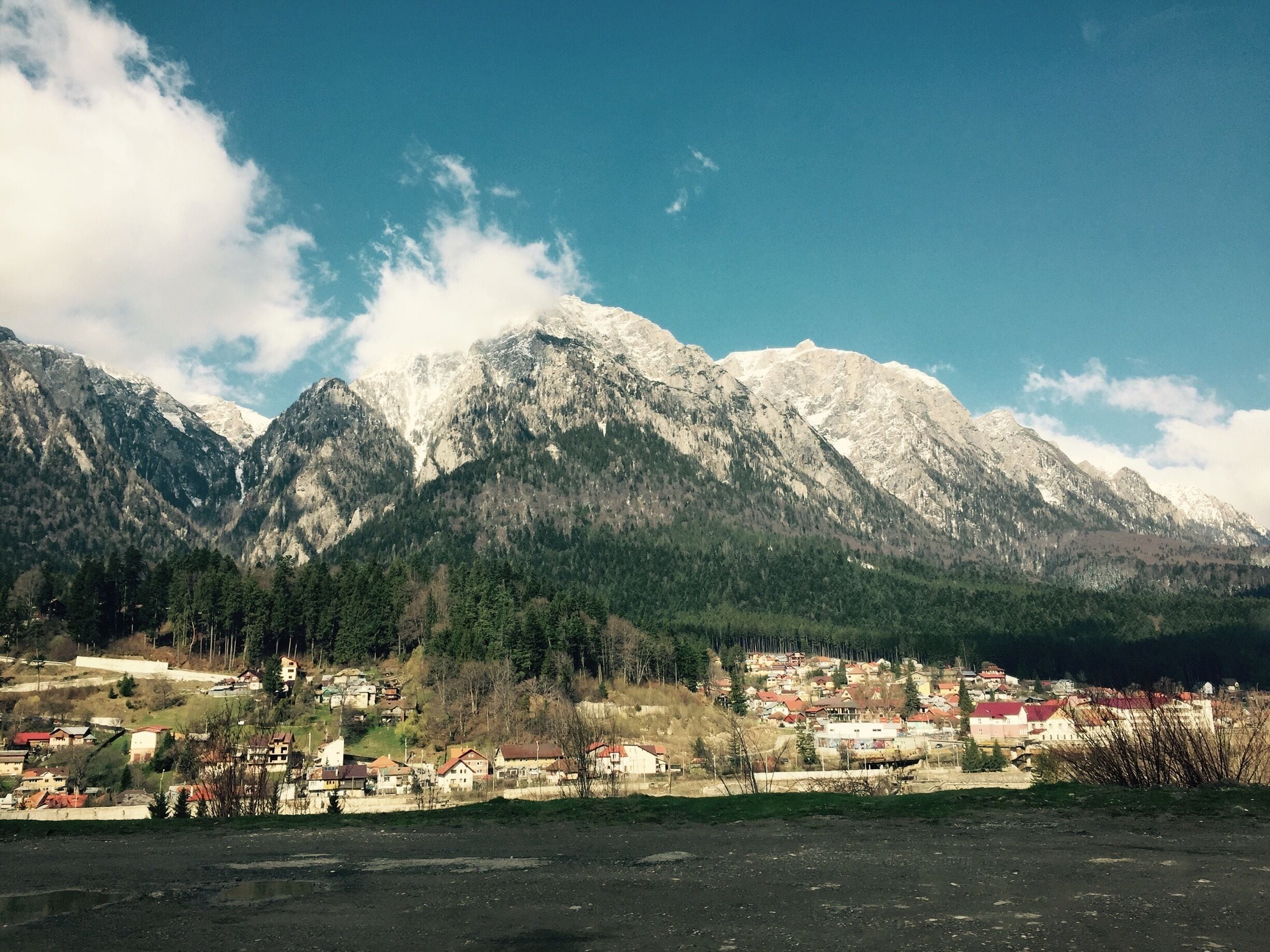 A mountain range with snow-capped peaks, a town with red-roofed houses, and a clear blue sky.