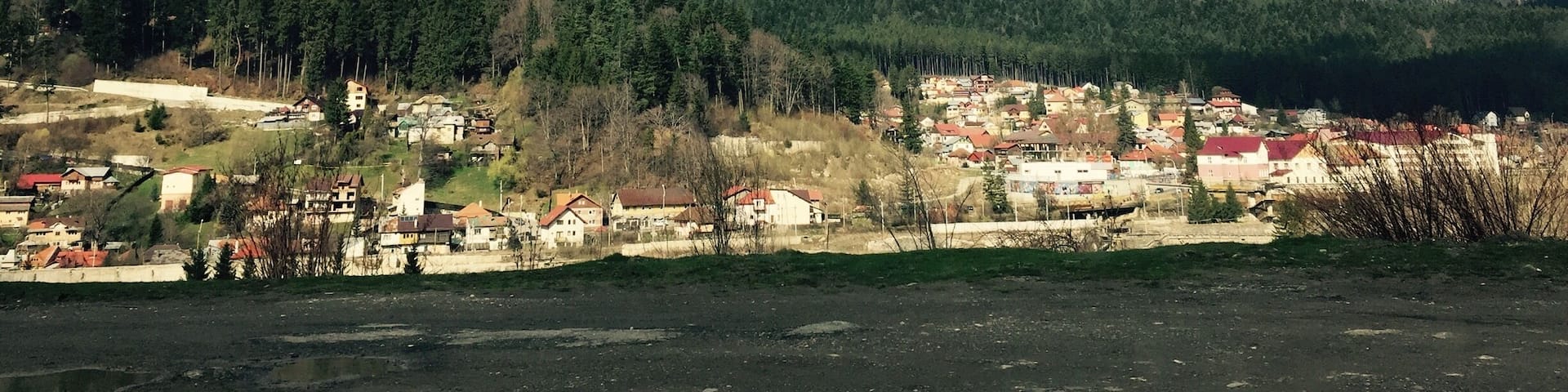A mountain range with snow-capped peaks, a town with red-roofed houses, and a clear blue sky.