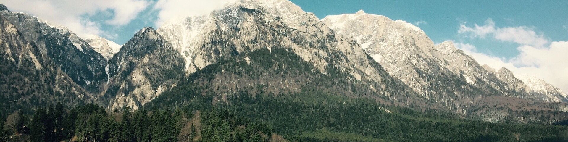 Una cadena montañosa con picos nevados, un pueblo con casas de tejados rojos y un cielo azul despejado.