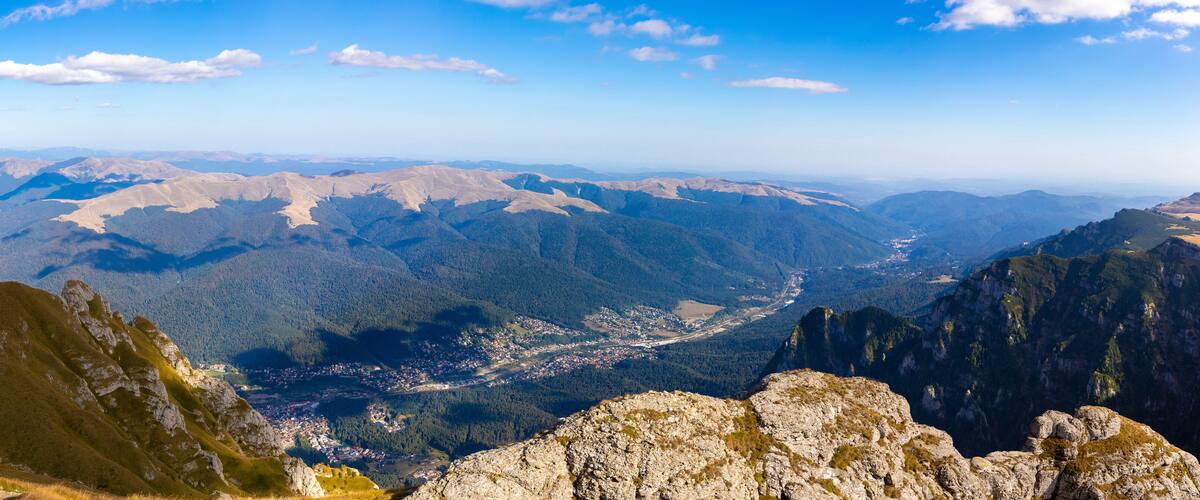 A mountainous landscape with a cross on a peak, a valley with a town, and distant mountains.
