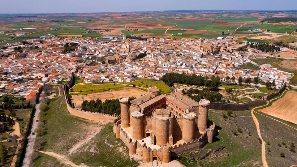 A medieval castle surrounded by a walled town with red-roofed buildings.