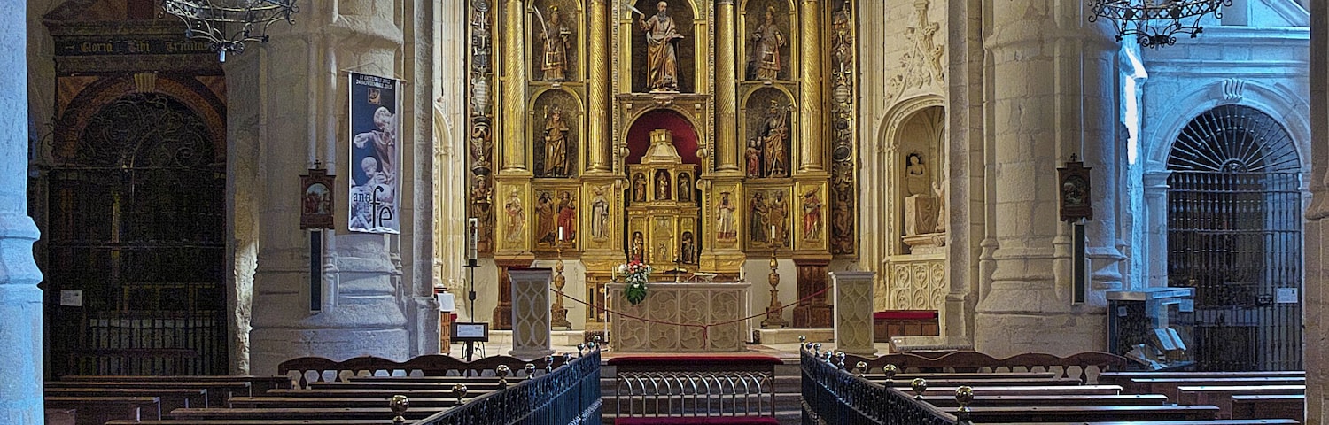 Interior de una catedral con techos altos de arco apuntado, un altar central y filas de bancas.