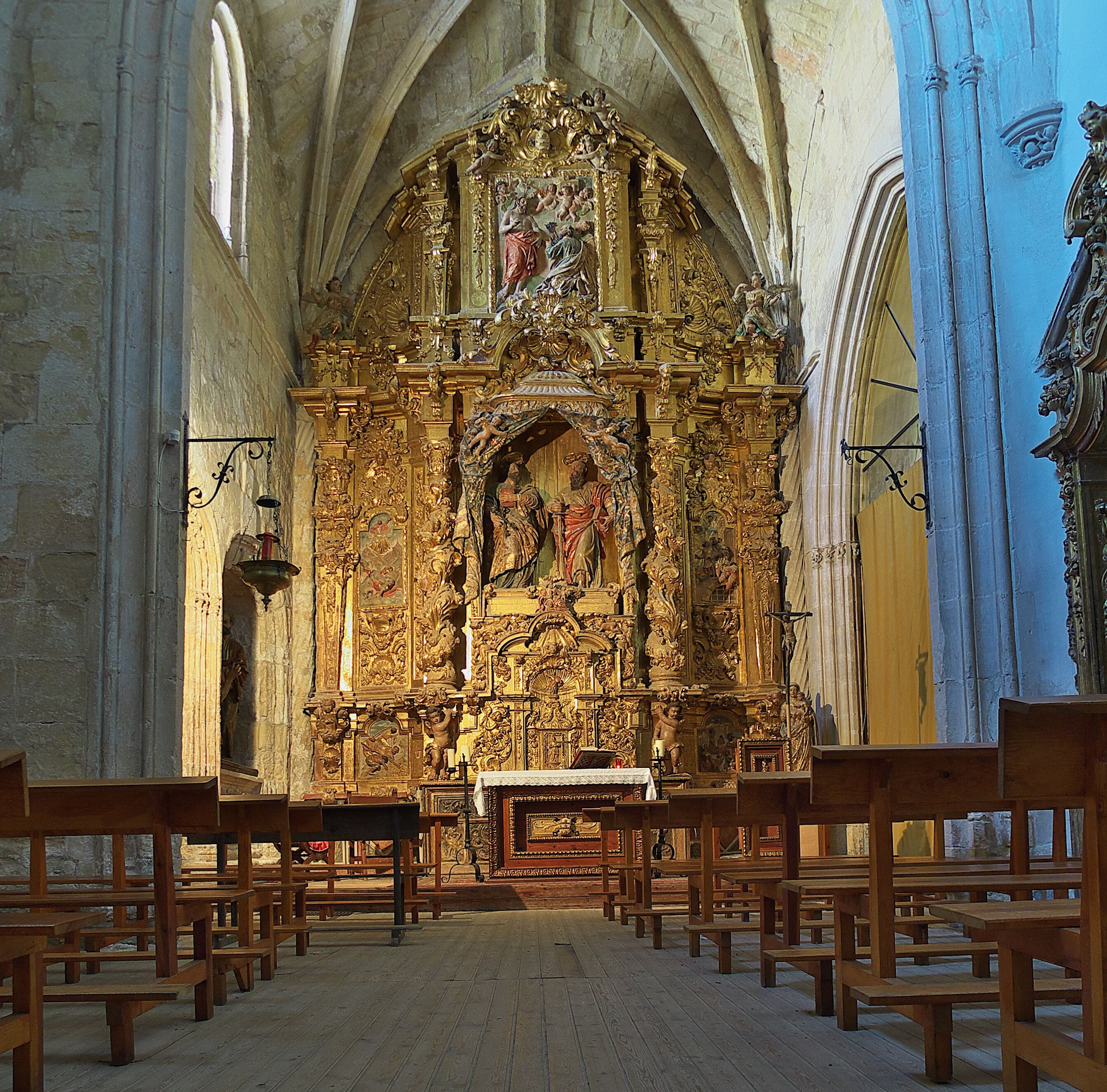 Interior ornamentado de una iglesia con un altar mayor, bancos de madera y arquitectura gótica.
