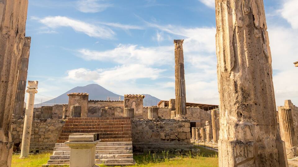Ancient ruins with columns and a staircase, with a mountain in the background.