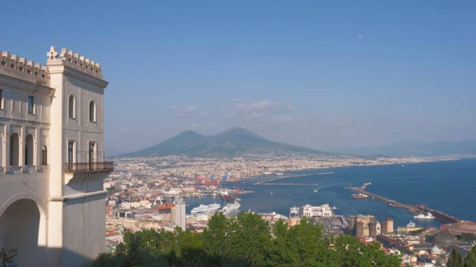 A coastal cityscape with a prominent tower, a clear view of the sea, and a distant mountain.